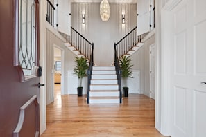 A wooden staircase with black railings, white walls, and two potted plants at the top.