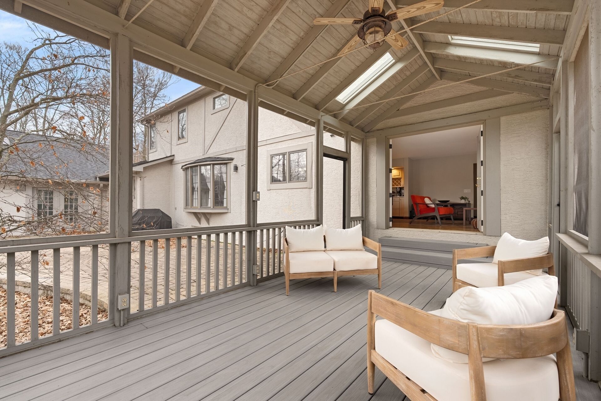 A covered porch with wooden furniture, a ceiling fan, and a view of a house.