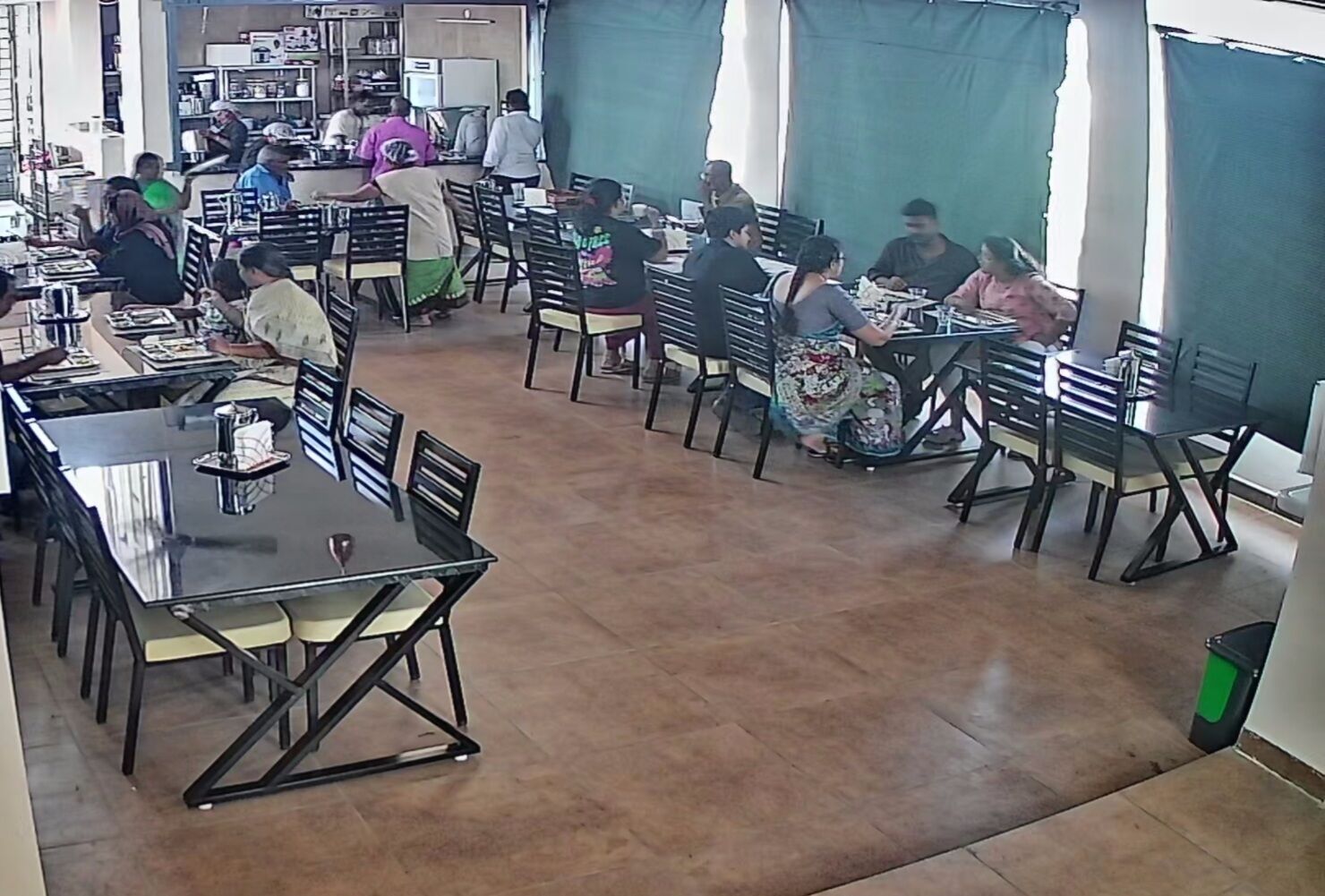 A restaurant with multiple tables and chairs, a tiled floor, and a kitchen area in the background.