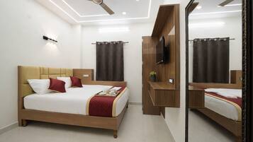 A hotel room with a bed, a ceiling fan, a TV, a mirror, and a bedside table.