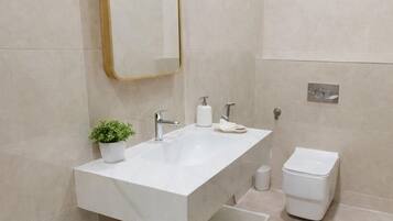 Un baño moderno con un espejo grande, un lavamanos blanco, una planta pequeña y un inodoro.