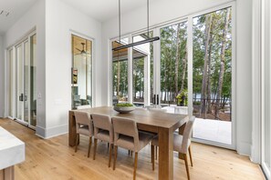 A modern dining area with a wooden table, six chairs, and a large window offering a view of trees and a deck. - Masters Week Reynolds Lake Oconee Luxury Lake Property in Richland Point Pool&HT (Greensboro)