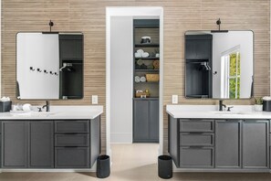 A modern bathroom with two sinks, dark cabinets, and a central shelving unit with towels and toiletries. - Masters Week Reynolds Lake Oconee Luxury Lake Property in Richland Point Pool&HT (Greensboro)