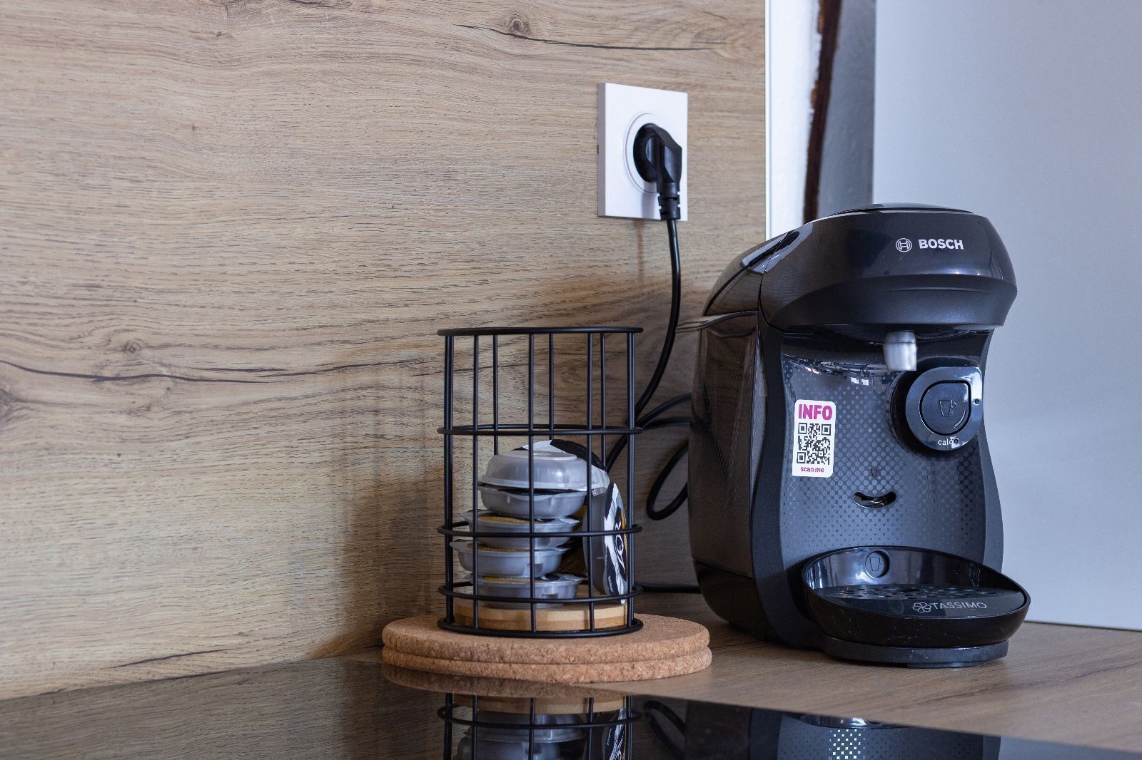 A coffee maker on a wooden surface with a power outlet in the background.