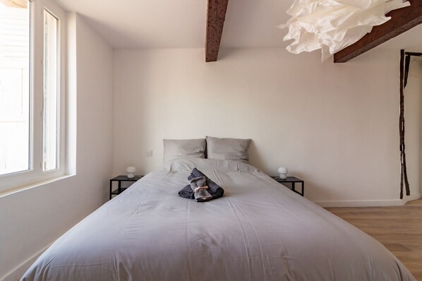 A bedroom with a bed, two bedside tables, a window, and a wooden ceiling beam.