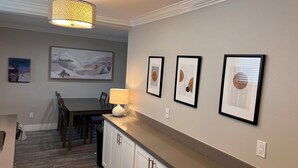 Un comedor con una mesa, sillas y una lámpara. Hay obras de arte enmarcadas en la pared.