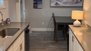 Una cocina moderna con suelo de madera, armarios blancos, una mesa de comedor y una lámpara colgante.