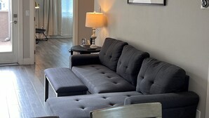 Una sala de estar moderna con un sofá seccional, un ventilador de techo, una lámpara y un cuadro en la pared.
