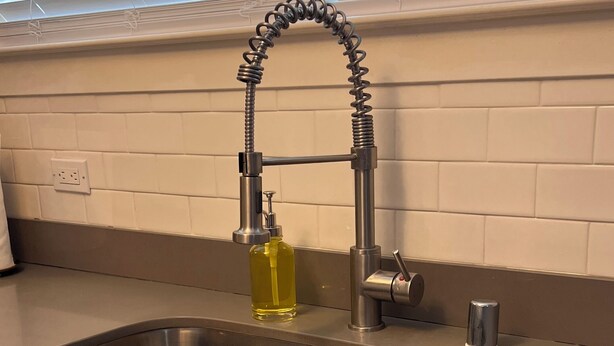 Un lavamanos de acero inoxidable con un grifo moderno, una botella de detergente y una lata de metal.