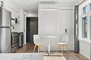 Una cocina moderna con electrodomésticos de acero inoxidable, una zona de comedor con dos sillas blancas y un ventanal con cortinas.