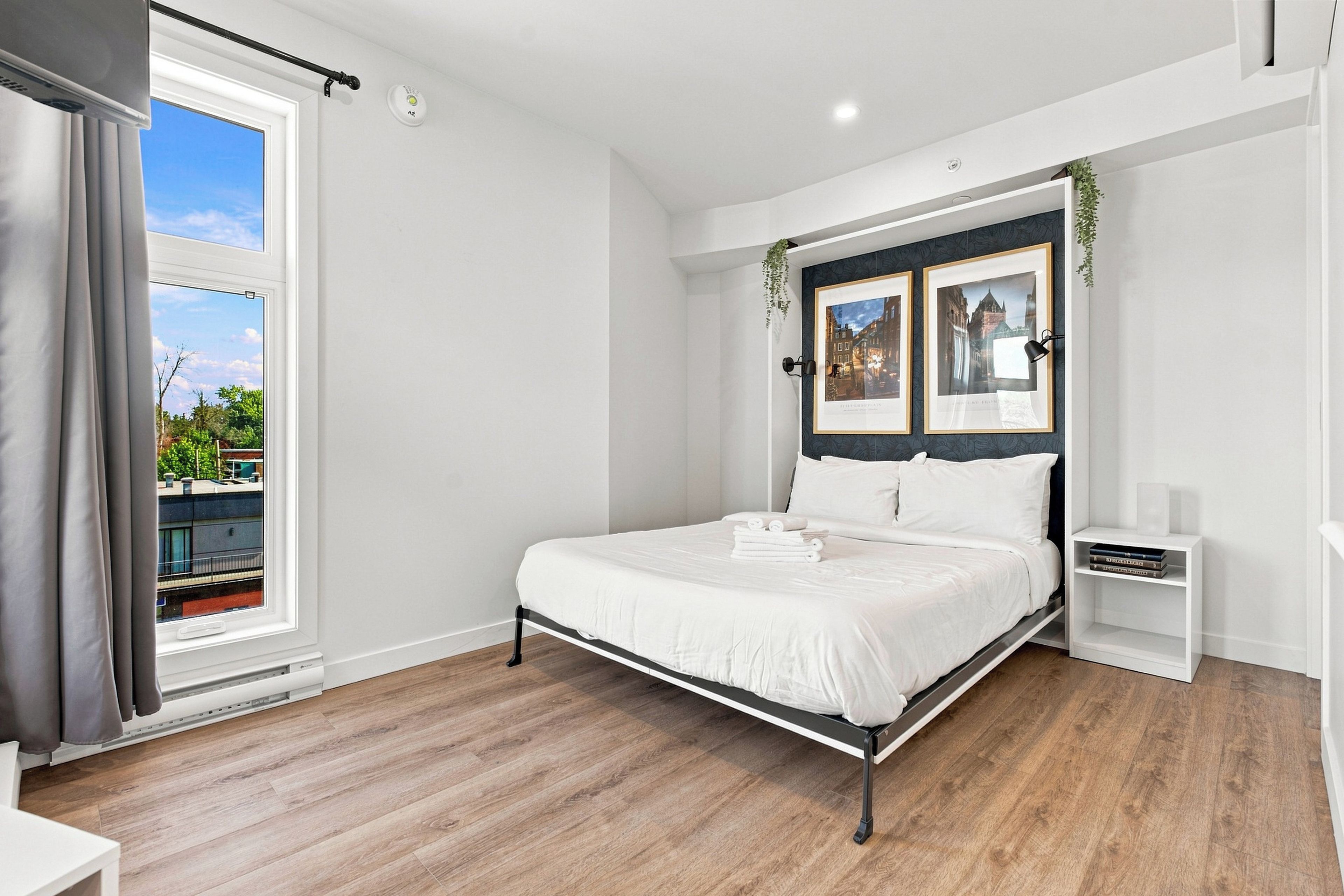Un dormitorio moderno con una cama grande, una mesita de noche, un armario pequeño y una ventana con cortinas.