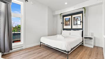 Un dormitorio moderno con una cama grande, una mesita de noche, un armario pequeño y una ventana con cortinas.