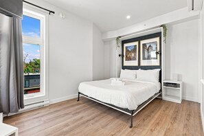 A modern bedroom with a large bed, a bedside table, a small cabinet, and a window with curtains. - Appart'hôtel Viveo - Par Aneyro (Québec)