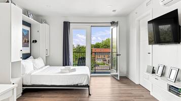 A modern bedroom with a bed, a TV, and a balcony with a view of buildings.