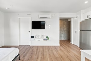 Un dormitorio moderno con una cama, un televisor de pantalla plana montado en la pared, un estante con objetos decorativos y suelo de madera.