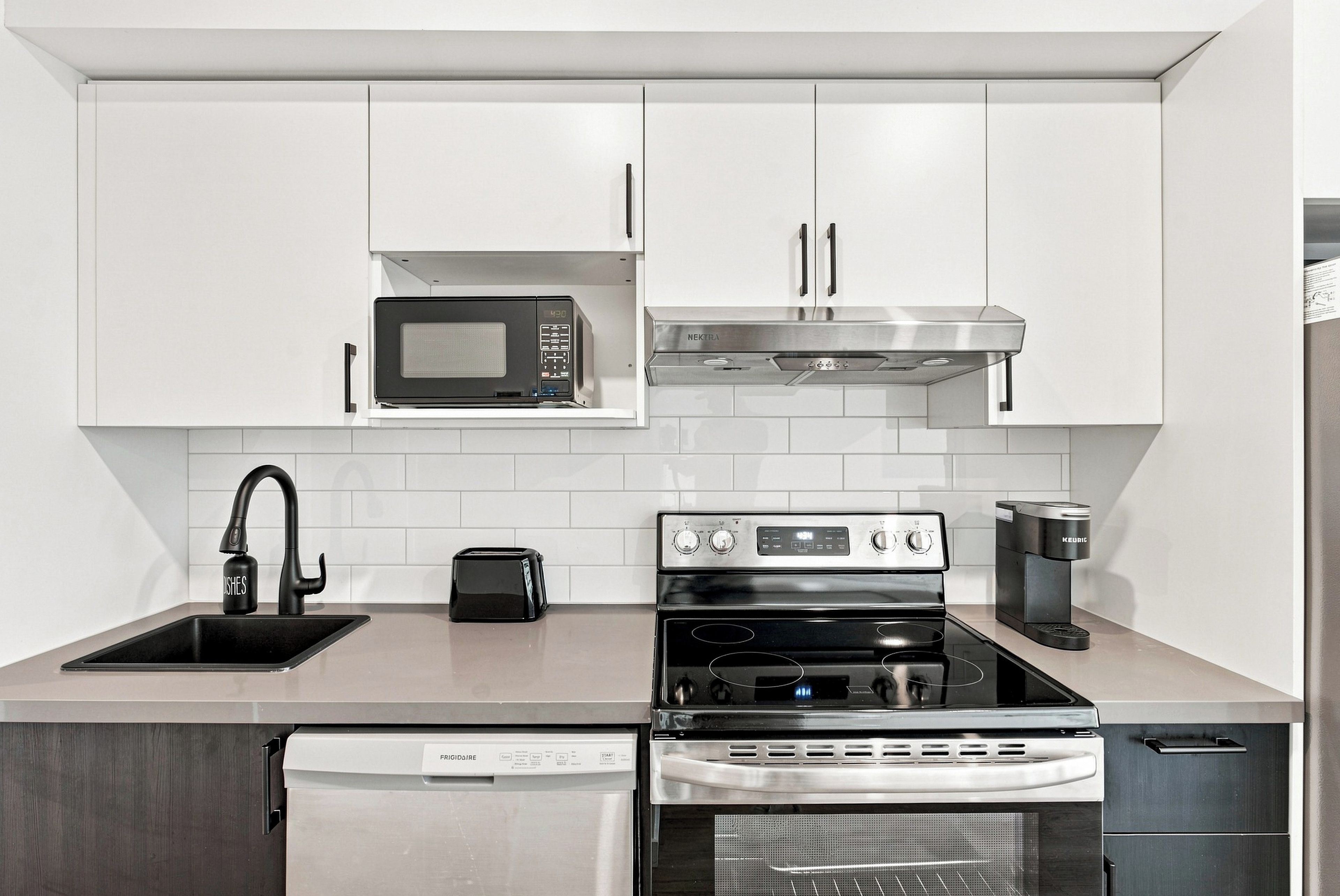 Una cucina moderna con mobili bianchi, forno a microonde integrato, cappa aspirante in acciaio inossidabile, tostapane, forno e lavastoviglie.
