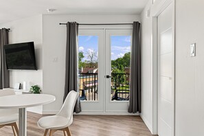 A modern room with a dining area, a flat-screen TV mounted on the wall, and a sliding glass door leading to an outdoor balcony. - Appart'hôtel Viveo - Par Aneyro (Québec)
