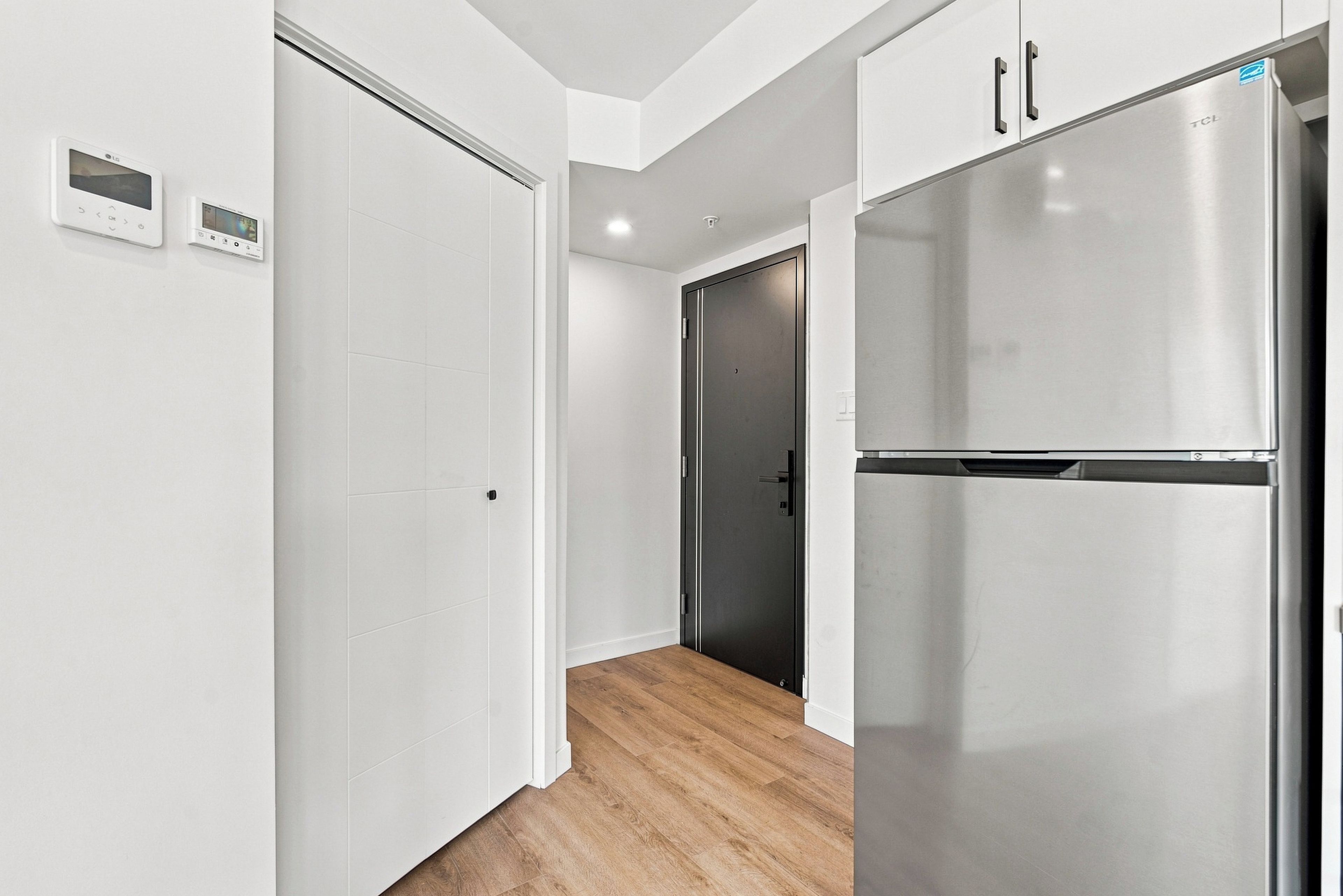 A modern kitchen with a stainless steel refrigerator, white cabinetry, and a wooden floor.