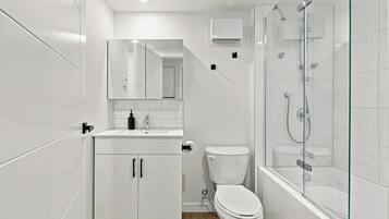 Une salle de bain moderne équipée de toilettes, d’une douche à parois de verre et d’un meuble-lavabo avec un miroir.