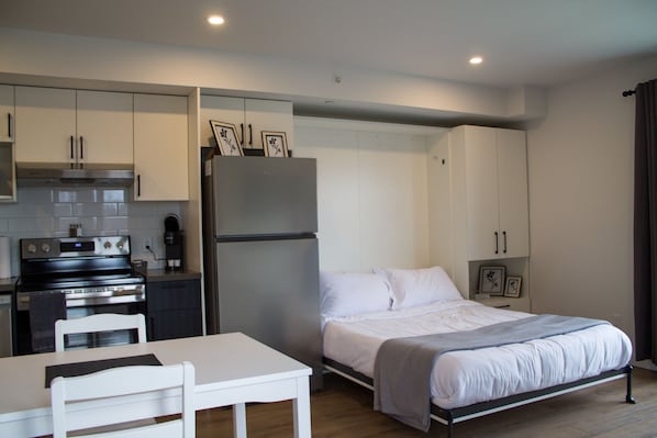 A compact hotel room with a kitchenette, a bed, a small table, and a chair. - Appart'hôtel Viveo - Par Aneyro (Québec)