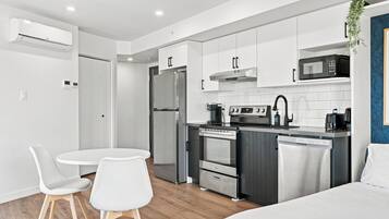 Une kitchenette moderne équipée d’un réfrigérateur, d’un four, d’un four à micro-ondes et d’une machine à café. Un petit coin repas est aménagé avec deux chaises et une table.