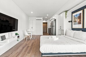 A modern bedroom with a bed, a desk, a TV, and a kitchenette. - Appart'hôtel Viveo - Par Aneyro (Québec)