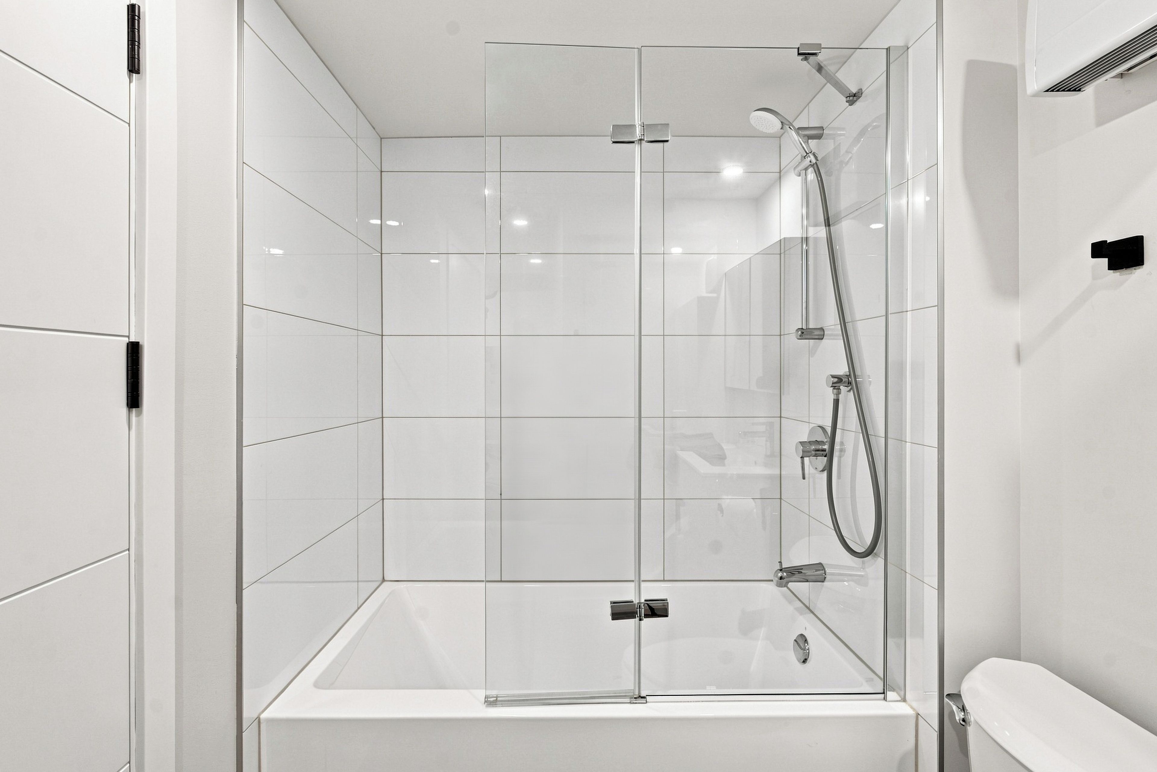 Un baño moderno con ducha envuelta en vidrio, una bañera blanca y un inodoro.