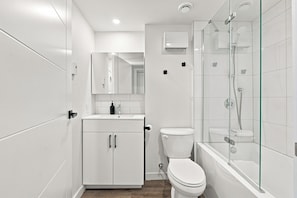 A modern bathroom with a toilet, a sink, a mirror, and a glass-enclosed shower area. - Appart'hôtel Viveo - Par Aneyro (Québec)
