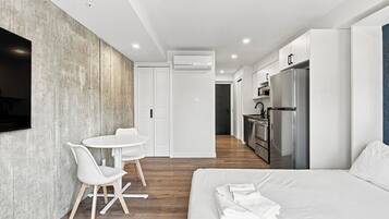 Une chambre d’hôtel moderne équipée d’un lit, d’un coin repas avec des chaises, d’une cuisine avec un réfrigérateur et d’un appareil de climatisation.