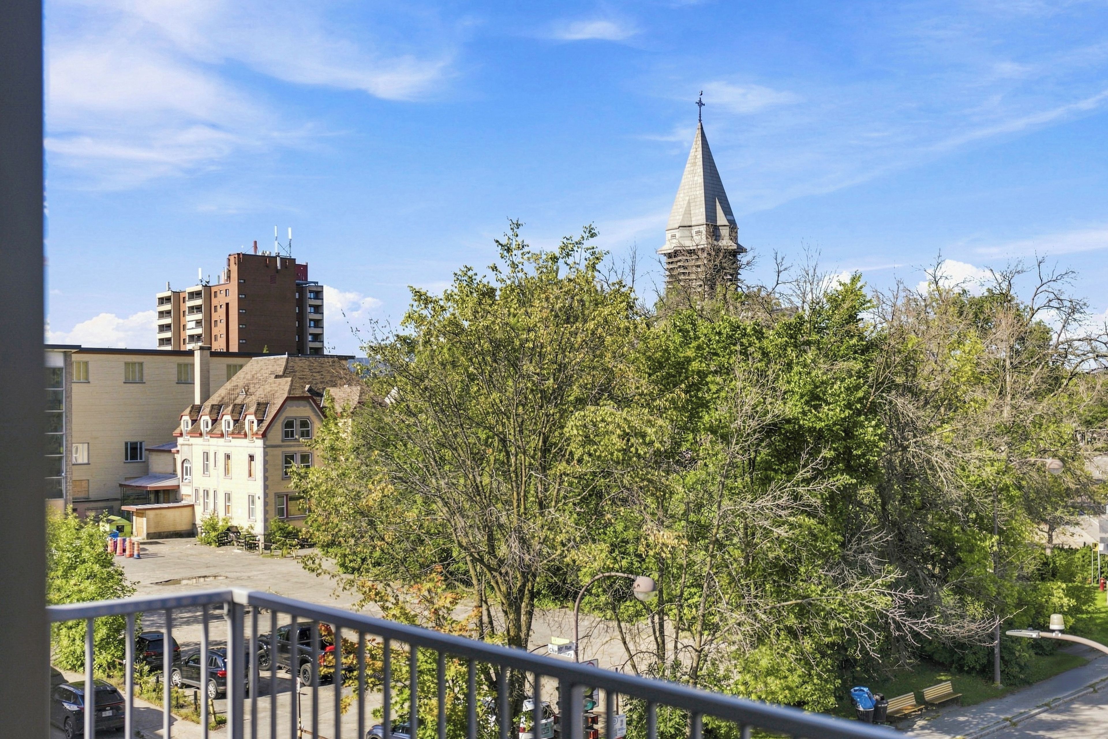 A residential area with a church steeple, a multi-story building, and a street with parked cars.