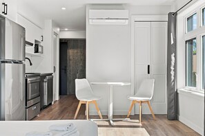 Una cocina moderna con electrodomésticos de acero inoxidable, una zona de comedor con dos sillas blancas y un ventanal con cortinas.