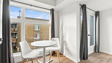 Una habitación moderna con un ventanal grande, dos sillas blancas y una mesita redonda.