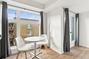 Una habitación moderna con un ventanal grande, dos sillas blancas y una mesita redonda.