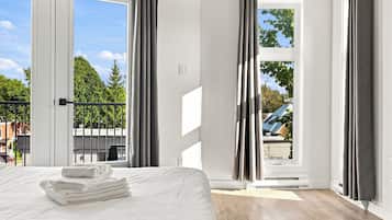 A hotel room with a bed, a window with curtains, a view of trees, and a balcony.
