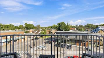 A balcony with a view of a parking lot, buildings, and trees.