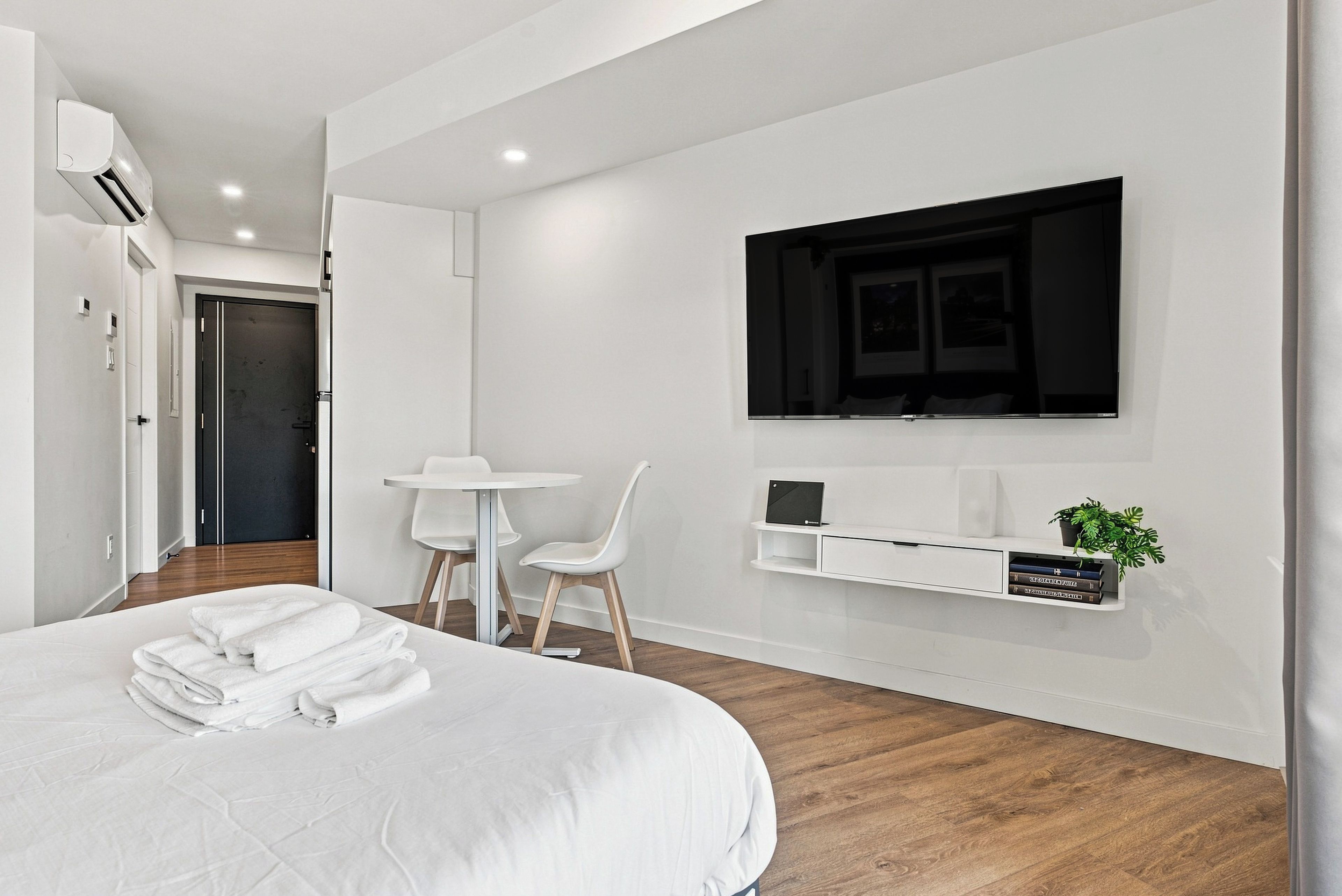 Una habitación de hotel moderna con una cama grande, un escritorio con dos sillas, un televisor montado y una planta pequeña en un estante.