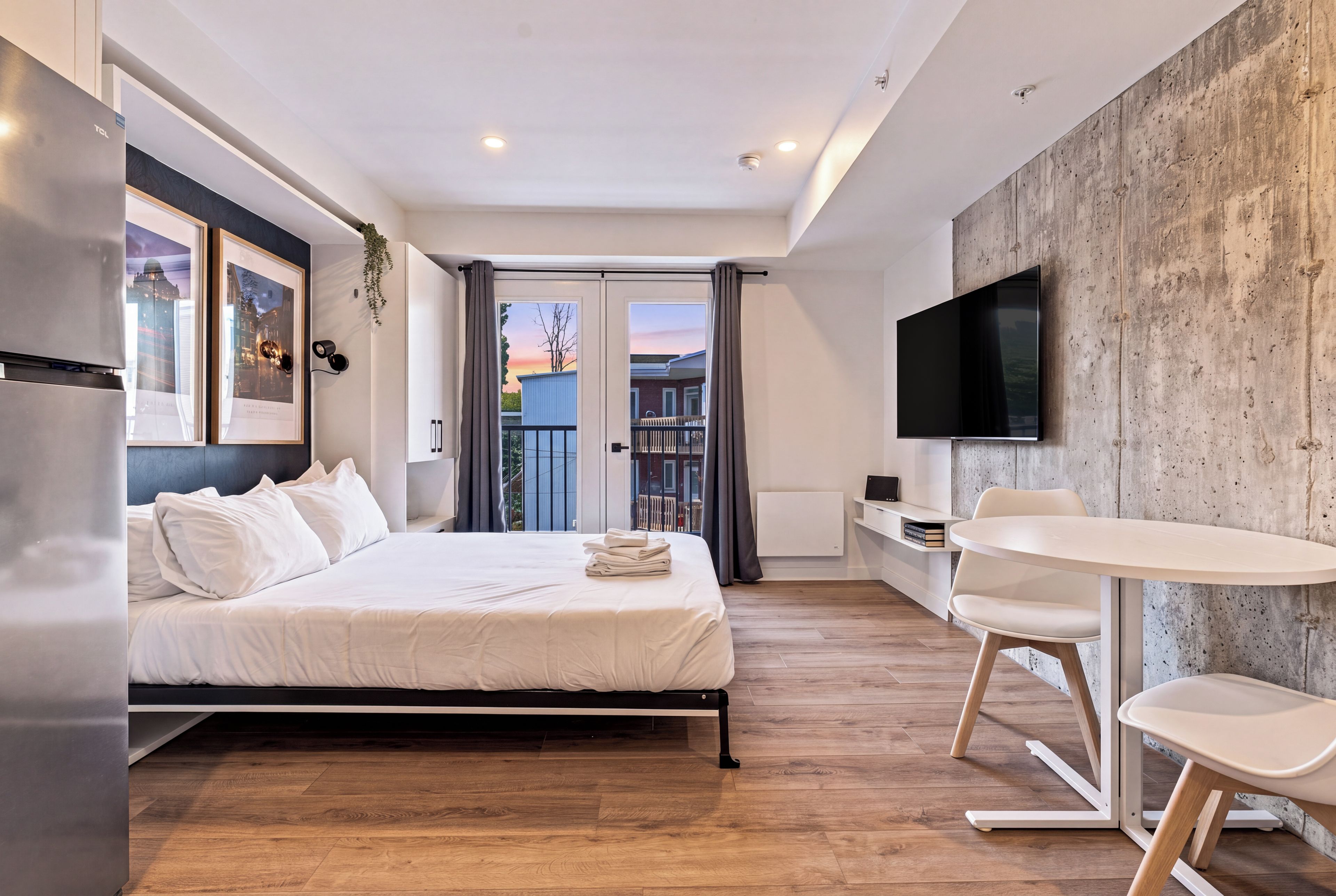 Une chambre d’hôtel moderne équipée d’un lit, d’un bureau, d’une chaise, d’un téléviseur à écran plat et d’un balcon avec vue.