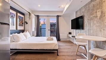 Une chambre d’hôtel moderne équipée d’un lit, d’un bureau, d’une chaise, d’un téléviseur à écran plat et d’un balcon avec vue.
