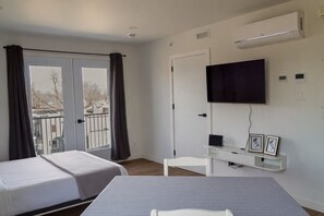 Una habitación con dos camas, un escritorio, una silla, un televisor y un balcón con cortinas.