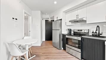 A modern kitchen with white cabinetry, a stainless steel refrigerator, an oven, and a microwave. There is a white dining table with chairs.