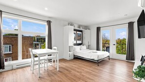 Quarto moderno com cama, escrivaninha e cadeira. Janelas amplas e varanda.