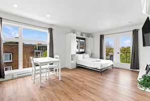 A modern bedroom with a bed, a desk, and a chair. There are large windows and a balcony. - Appart'hôtel Viveo - Par Aneyro (Québec)
