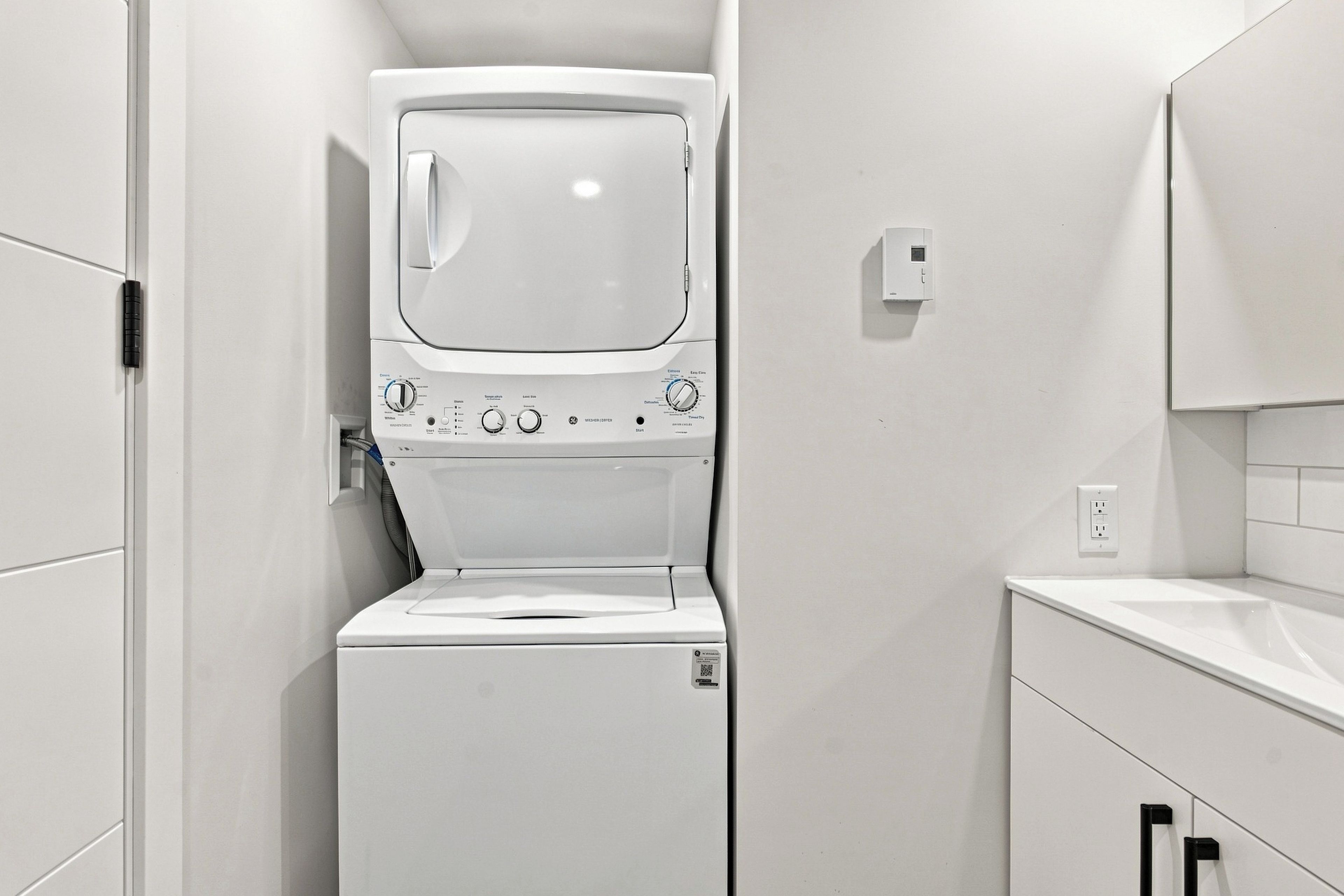 A compact, white laundry room with a front-loading washing machine and dryer, a small countertop, and a wall-mounted electrical outlet.