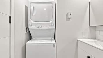 A compact, white laundry room with a front-loading washing machine and dryer, a small countertop, and a wall-mounted electrical outlet.