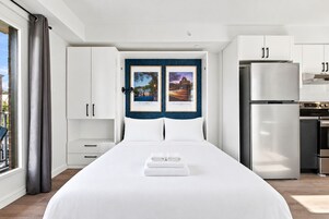 Habitación de hotel con una cama grande, vistas a la ciudad, kitchenette y un cuadro en la pared.