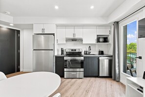 Una cocina moderna con electrodomésticos de acero inoxidable, un comedor con mesa blanca y vistas a zonas verdes a través de un ventanal corredero.