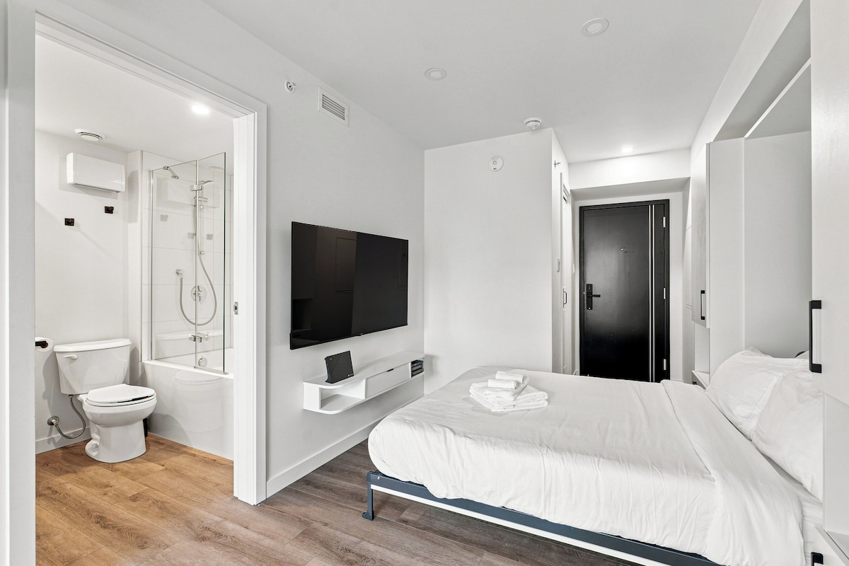 A modern bedroom with a large bed, a flat-screen TV, a built-in shower, and a separate toilet.
