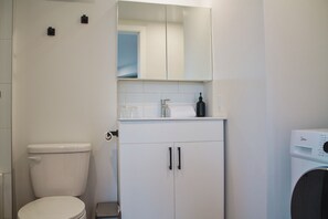 A bathroom with a toilet, a washing machine, a mirror, and a cabinet. - Appart'hôtel Viveo - Par Aneyro (Québec)