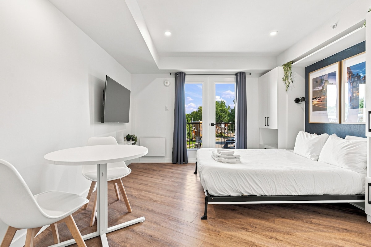 A modern bedroom with a bed, a desk, chairs, and a TV.