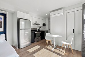 A modern kitchen with a refrigerator, stove, microwave, and a small dining area with two chairs. - Appart'hôtel Viveo - Par Aneyro (Québec)